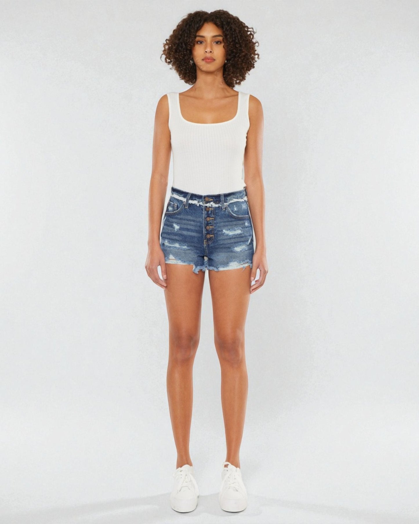 Person wearing a white tank top and blue denim shorts on a white background