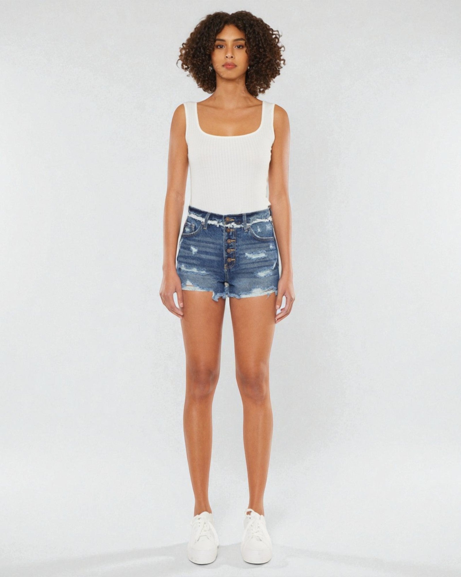 Person wearing a white tank top and blue denim shorts on a white background