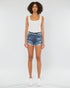 Person wearing a white tank top and blue denim shorts on a white background