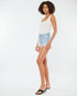 Woman wearing a white tank top and light blue denim shorts on a white background