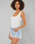 Woman wearing a white tank top and light blue denim shorts on a gray background