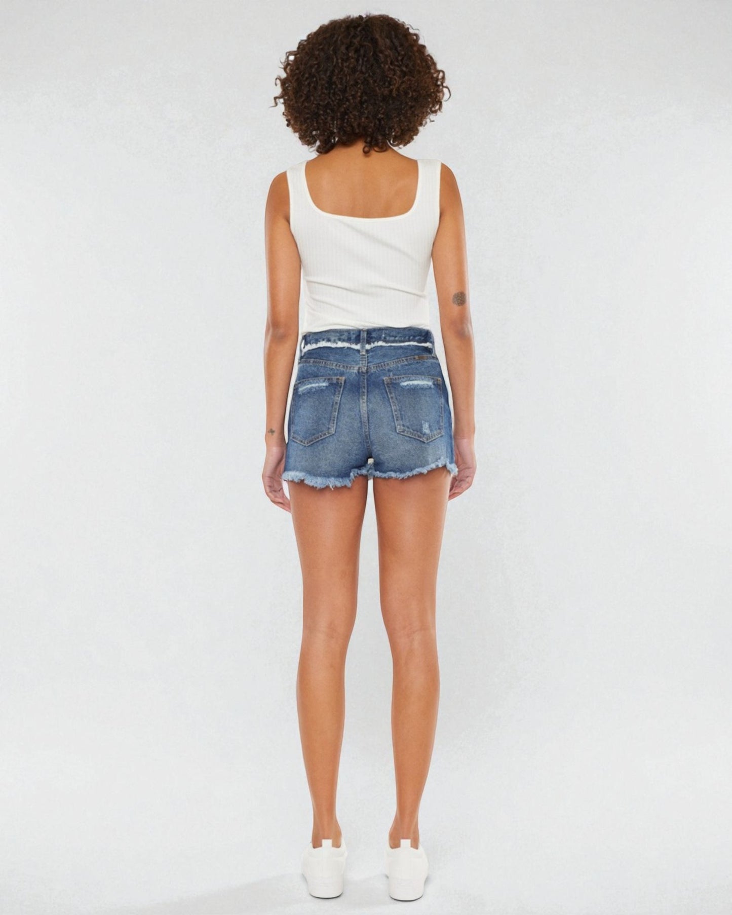 Person wearing a white tank top and denim shorts on a plain background