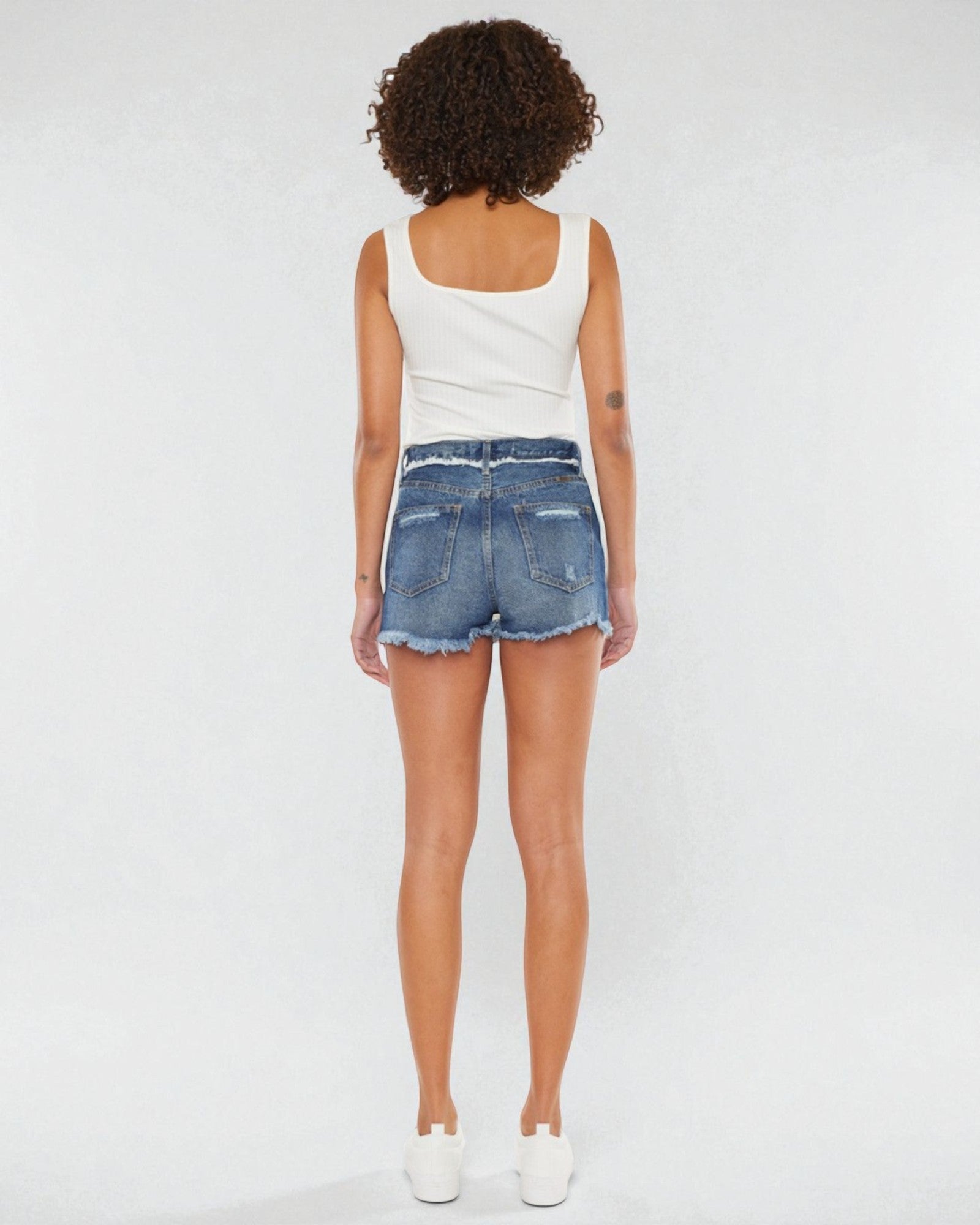 Person wearing a white tank top and denim shorts on a plain background