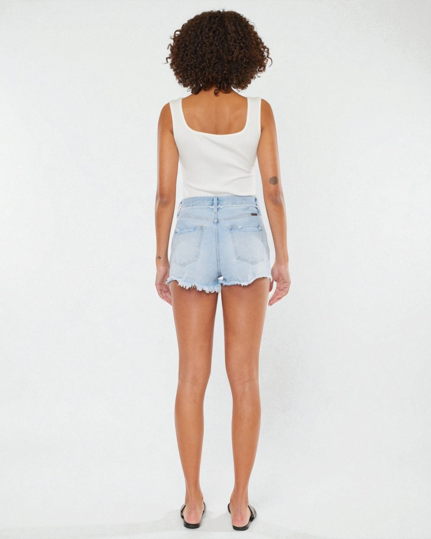 Person wearing a white tank top and light blue denim shorts on a white background