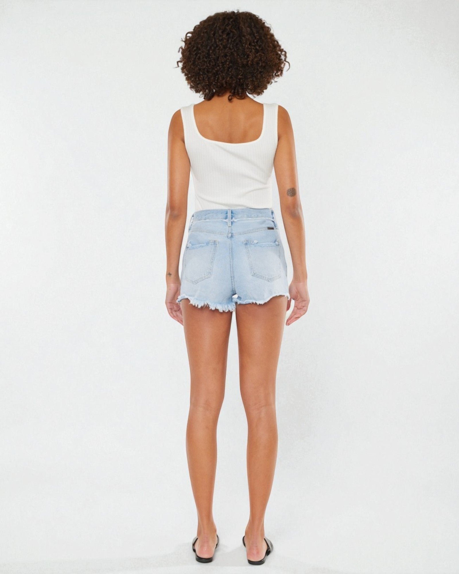 Person wearing a white tank top and light blue denim shorts on a white background