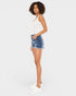 A woman modeling a white sleeveless tank top and distressed blue denim shorts against a light gray studio background.