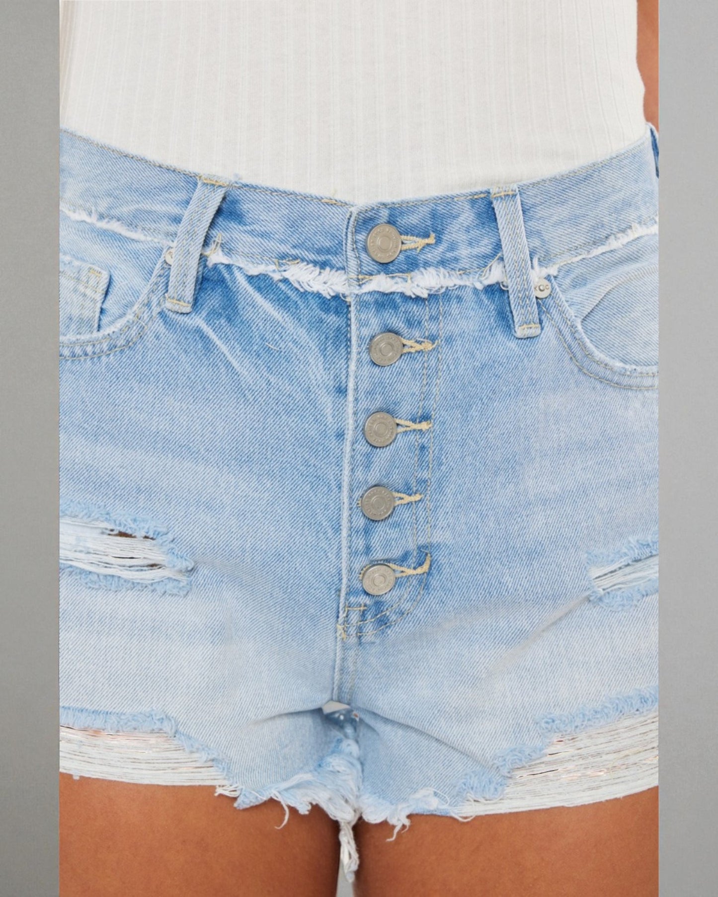 Close-up of light blue denim shorts with button details on a neutral background