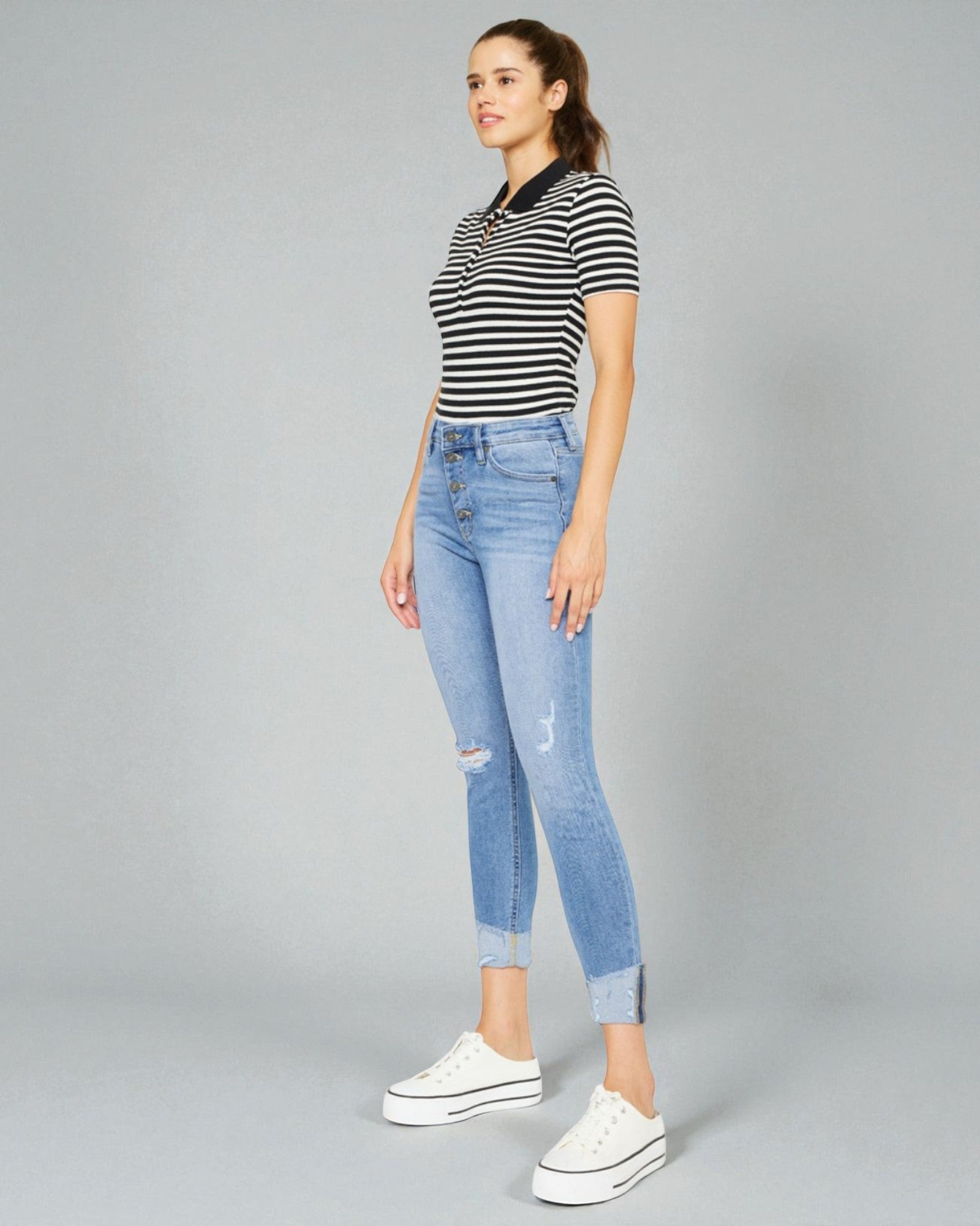 Woman wearing a striped shirt and ripped jeans on a gray background