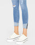 Ripped blue jeans with rolled-up cuffs worn with white sneakers on a light gray background