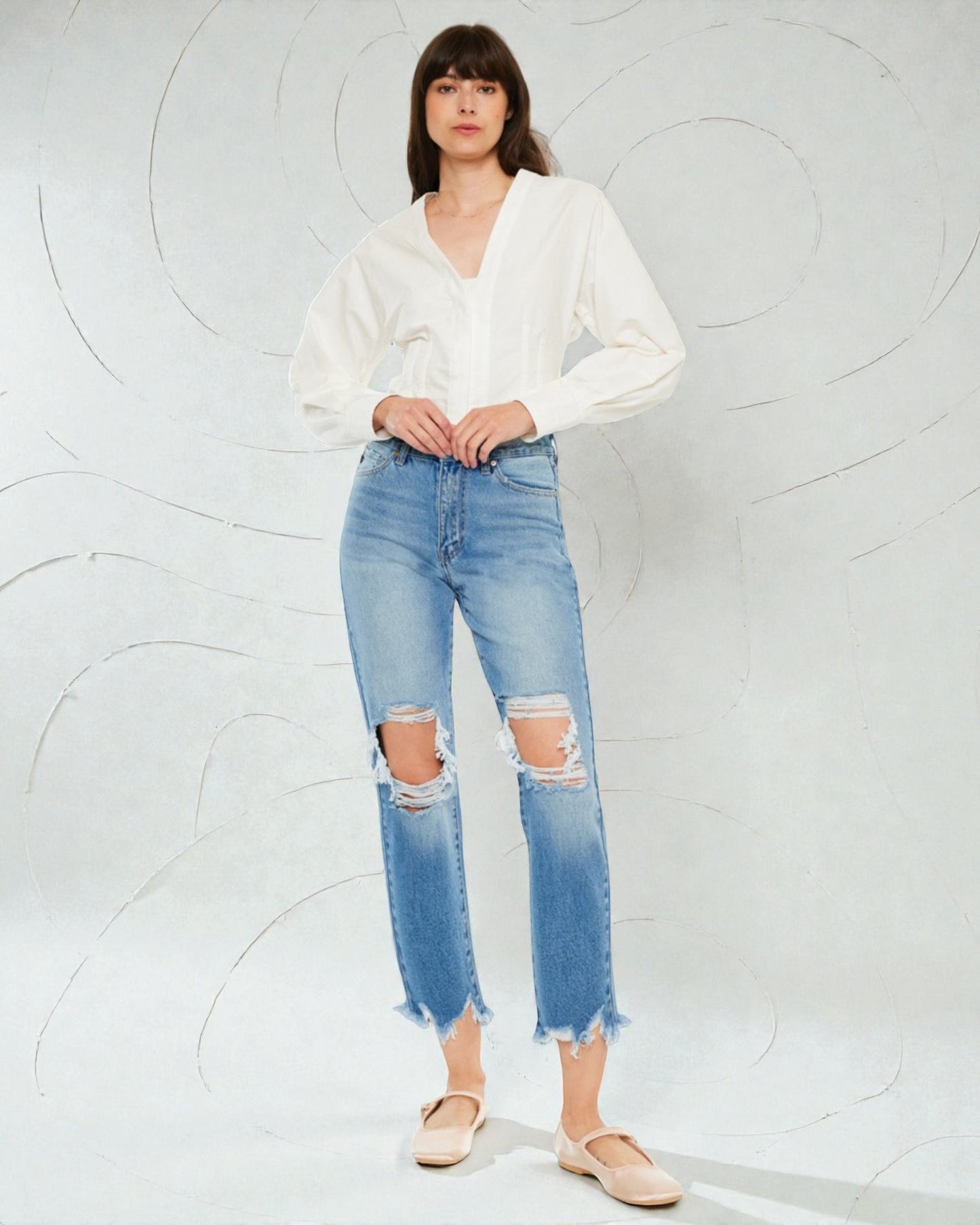 Woman wearing a white blouse and distressed blue jeans against a light gray background