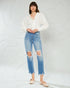 Woman wearing a white blouse and distressed blue jeans against a light gray background