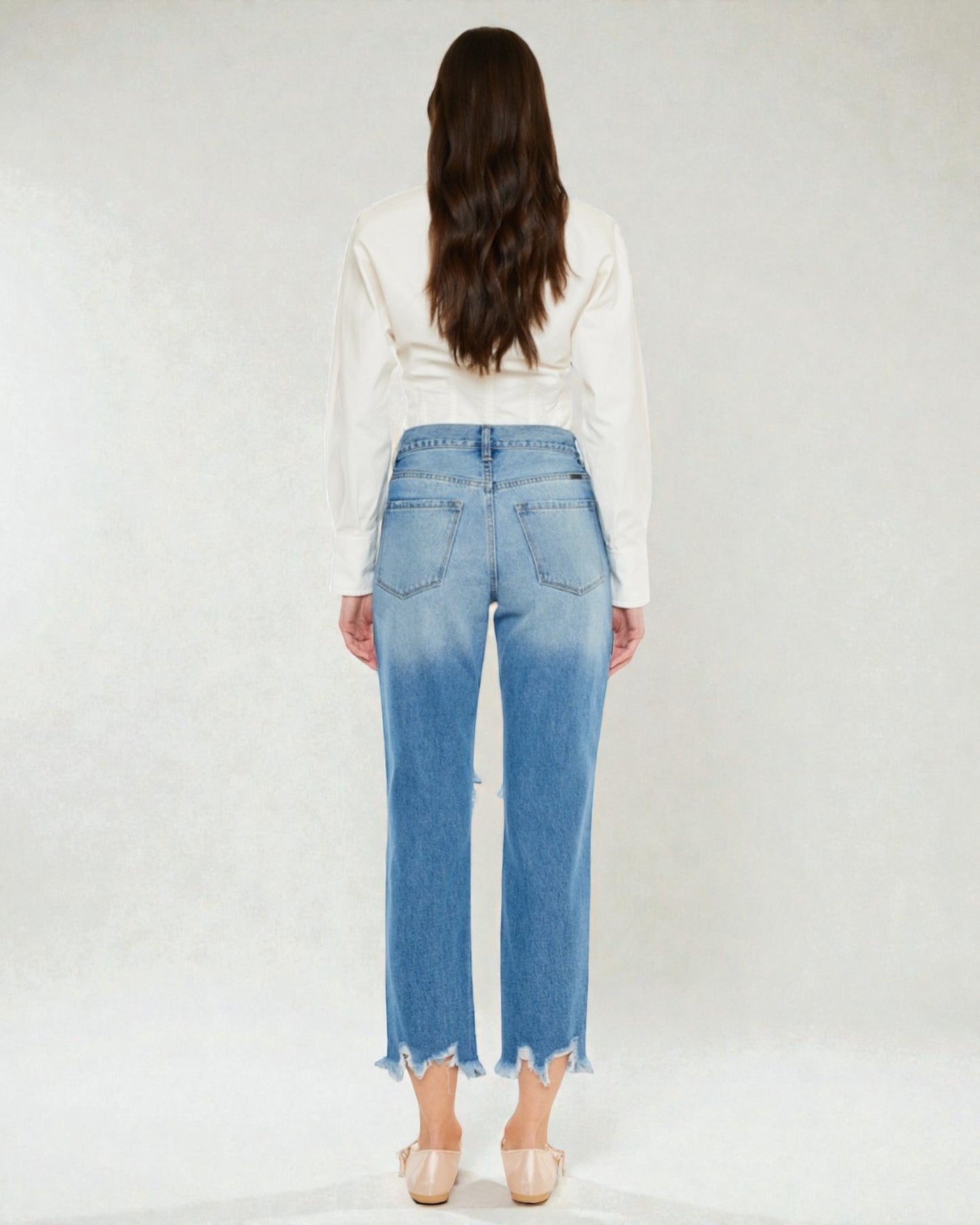 Person wearing blue jeans and a white top on a plain background