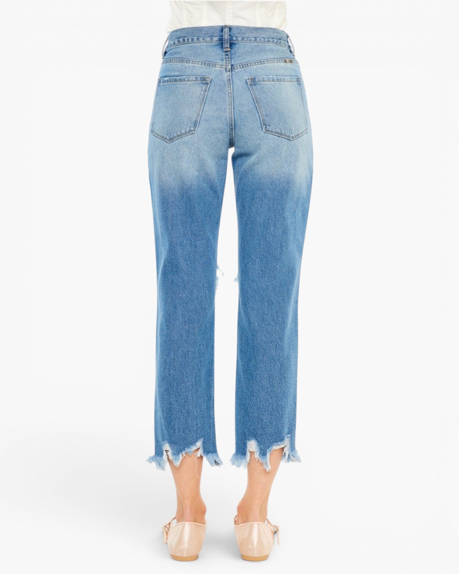 Back view of a model wearing light blue cropped jeans with a raw frayed hem and beige flat shoes, shown against a plain white background.