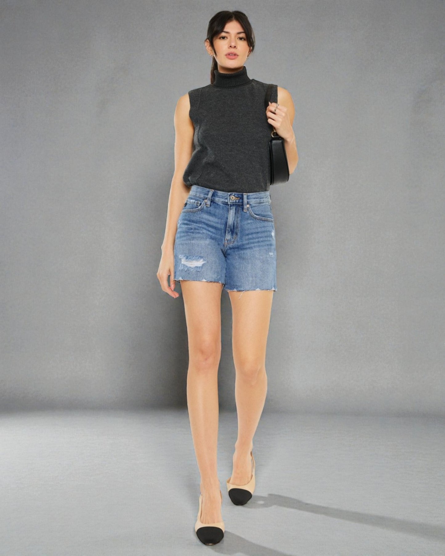 Woman wearing a black sleeveless top and denim shorts against a gray background