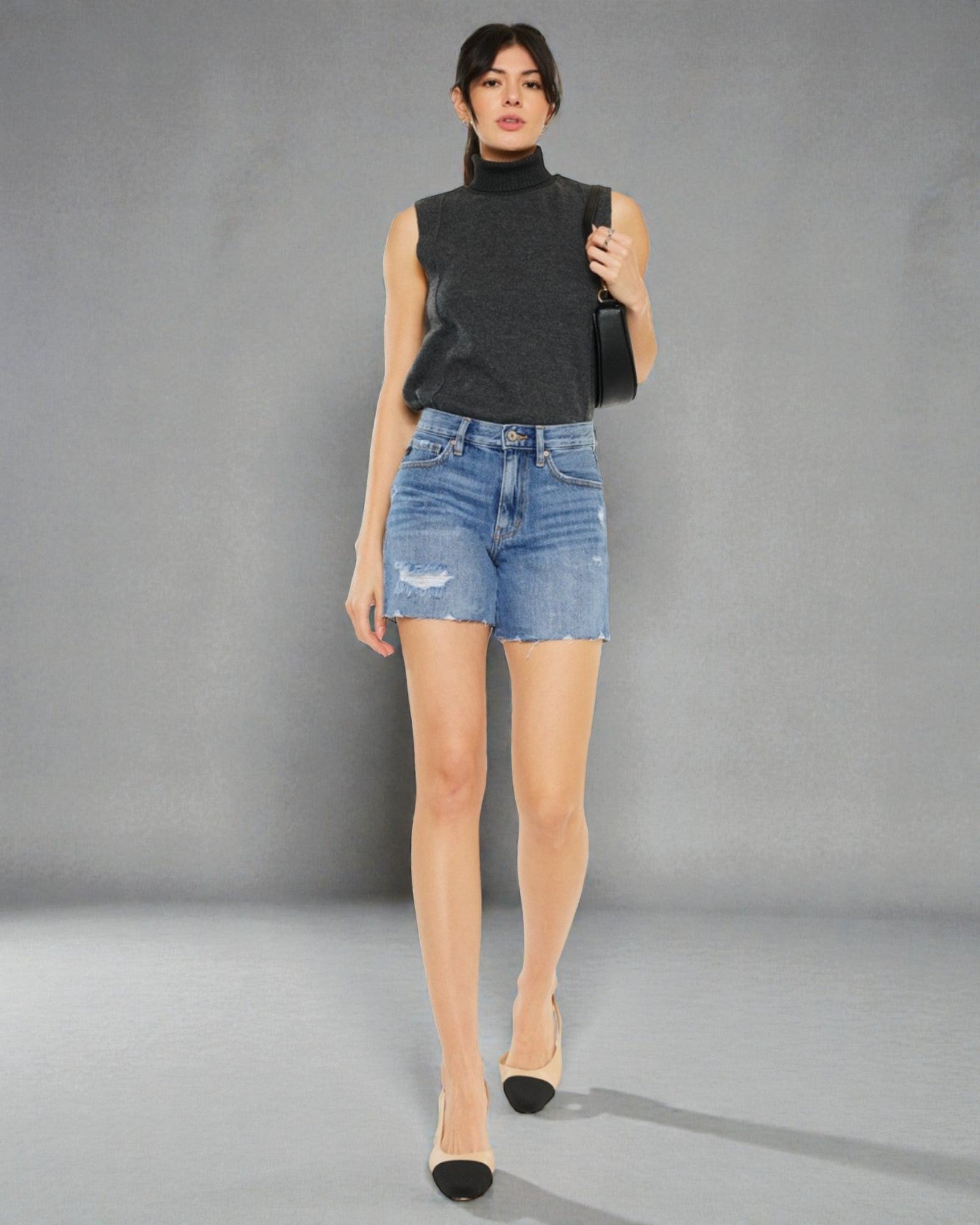 Woman wearing a black sleeveless top and denim shorts against a gray background