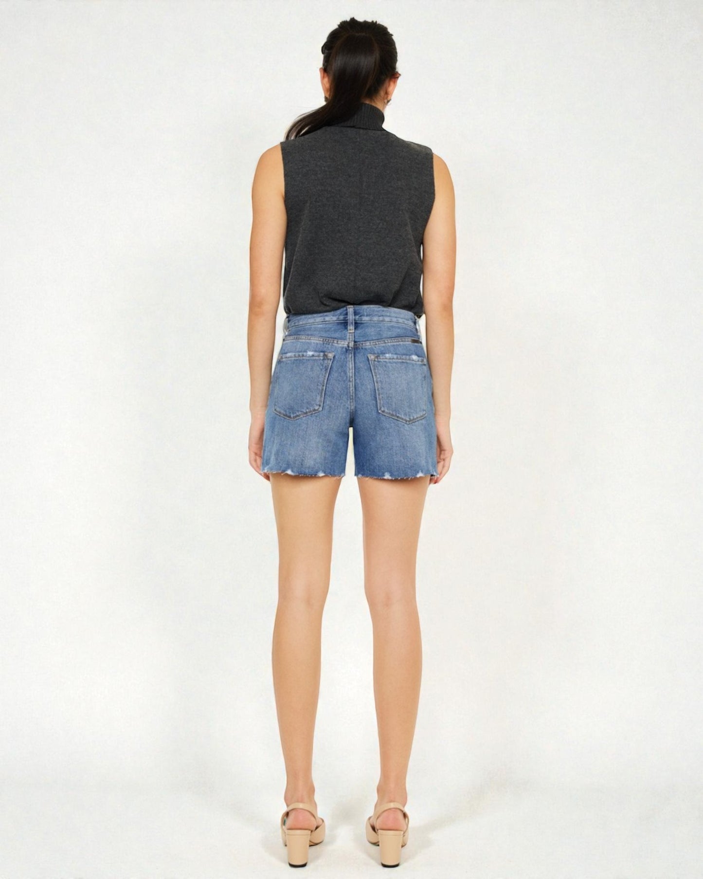 Person wearing a black sleeveless top and blue denim shorts on a white background