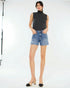 Woman wearing a black sleeveless top and blue denim shorts on a white background