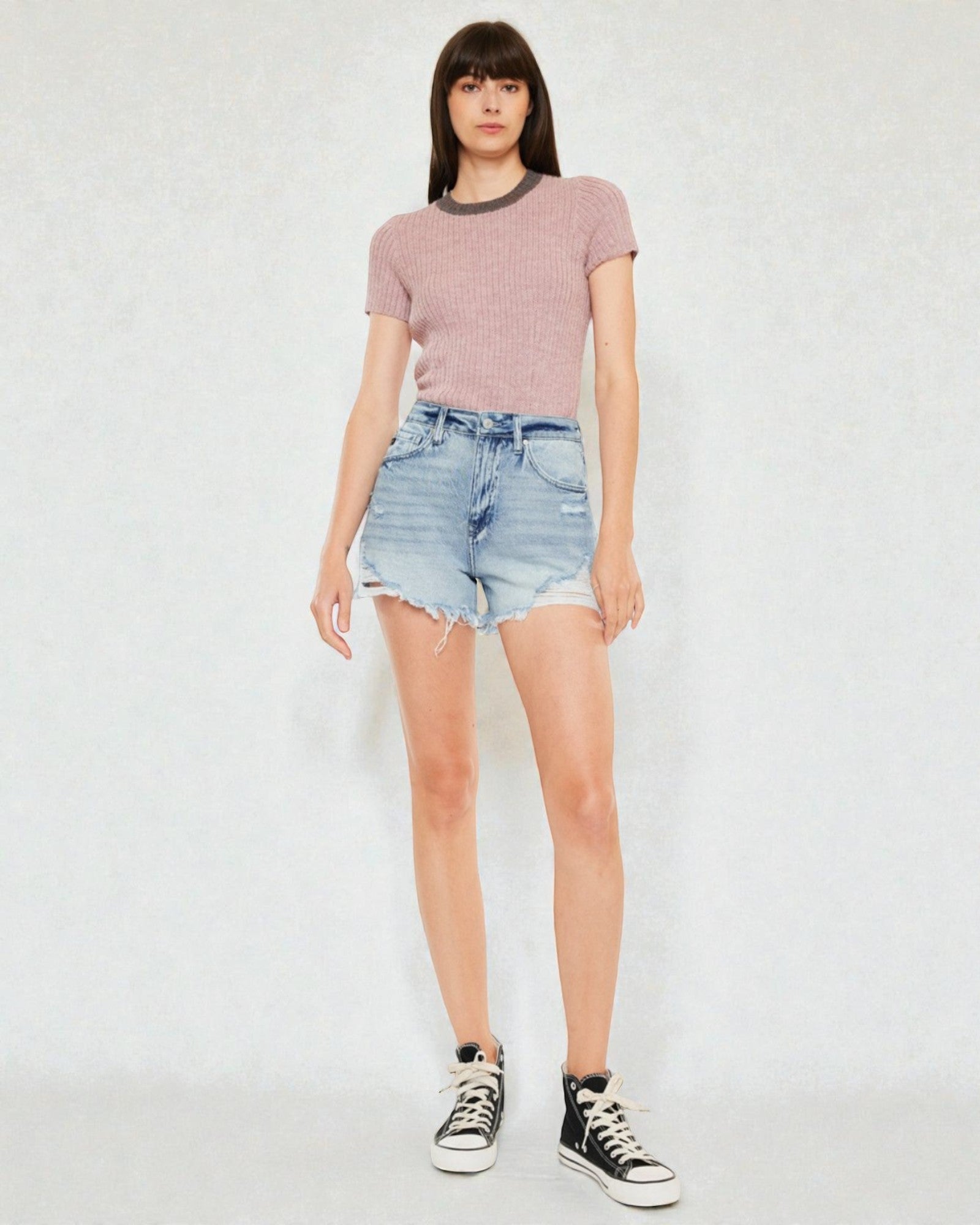 Person wearing a pink ribbed sweater and denim shorts on a white background