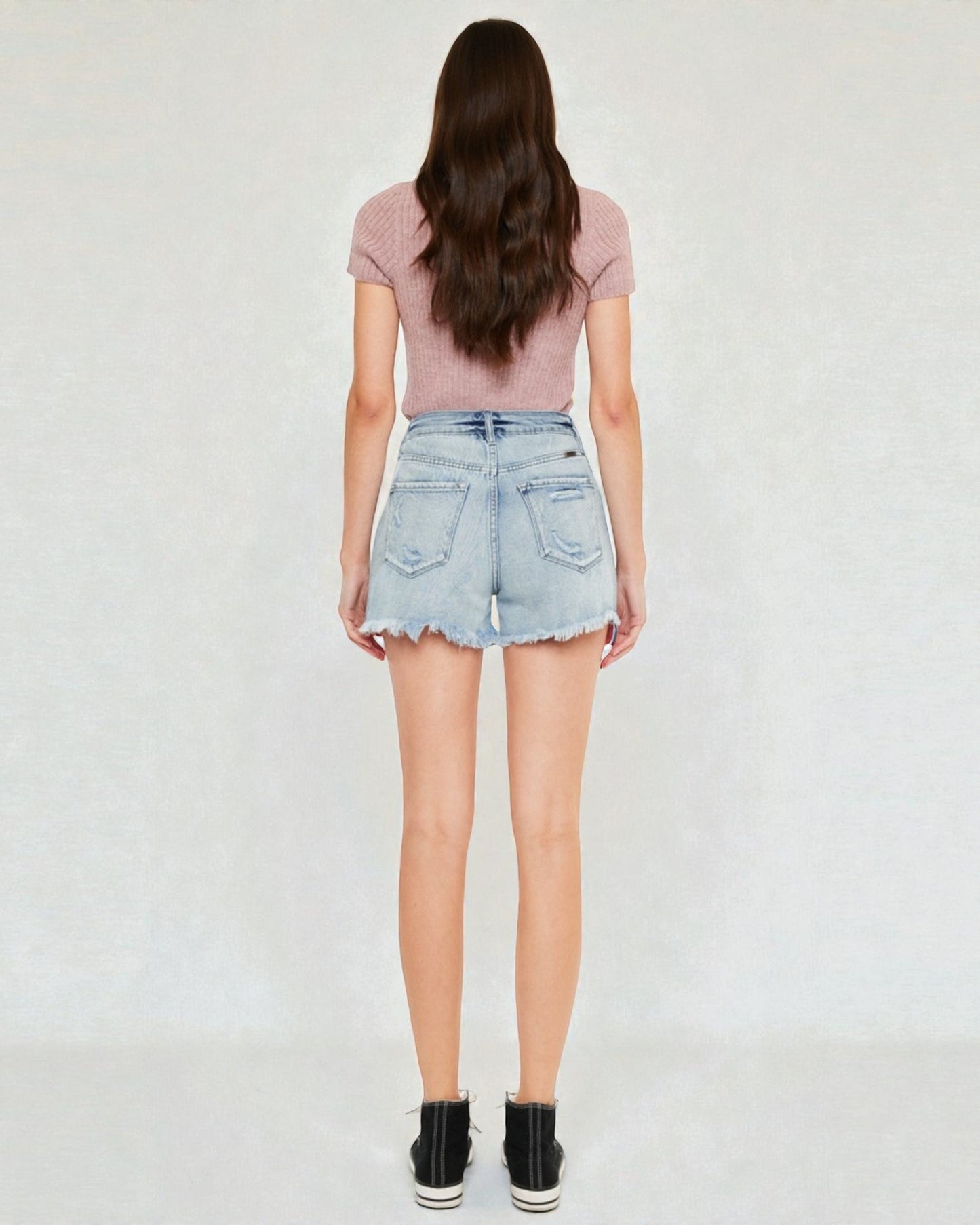 Person wearing a pink top and light blue denim shorts on a white background