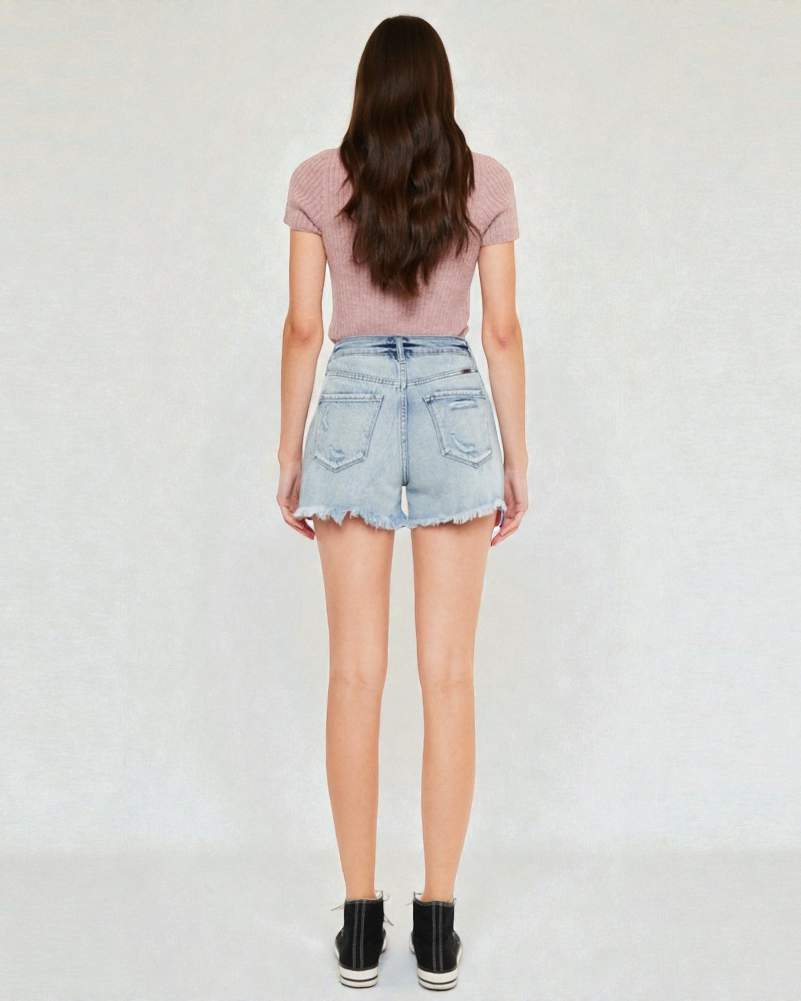 Person wearing a pink top and light blue denim shorts on a white background