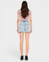 A model shown from the back wearing a light pink short-sleeve top, light-wash denim cut-off shorts, and black sneakers against a light gray studio background.