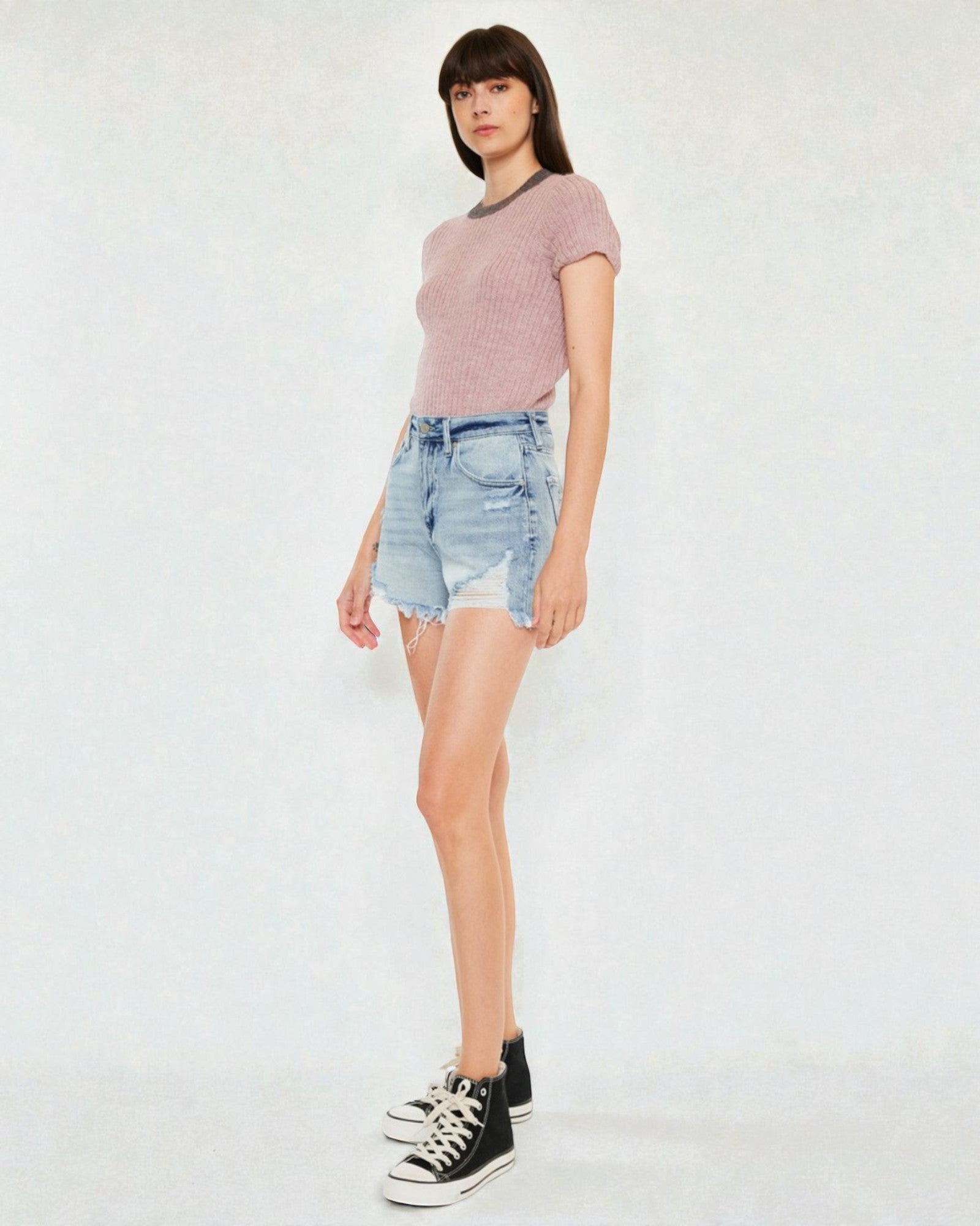 Woman wearing a pink t-shirt and denim shorts on a white background