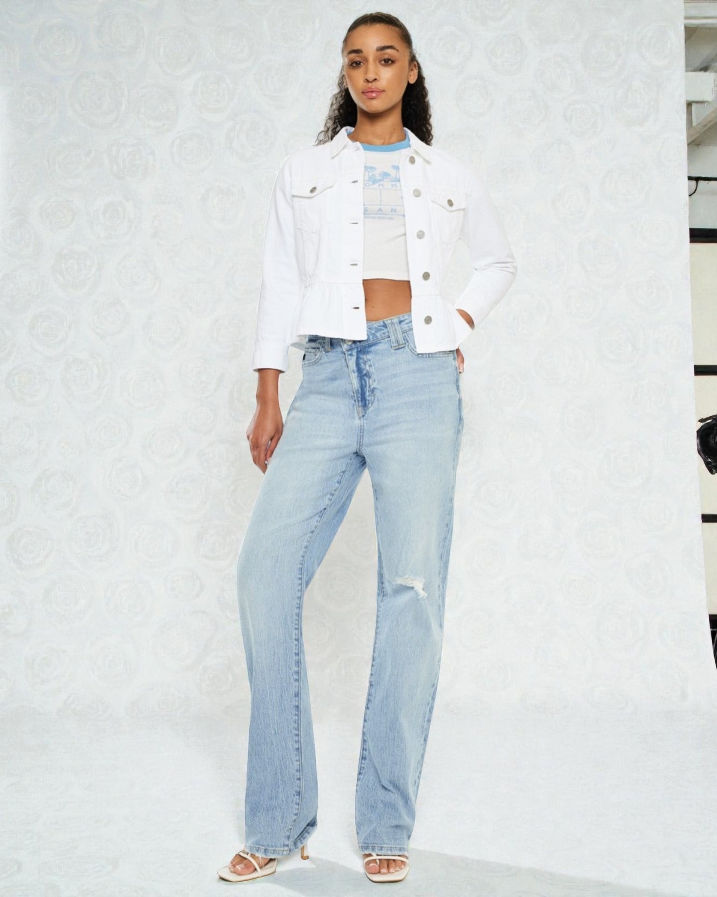 Woman wearing a white denim jacket and light blue jeans against a white background