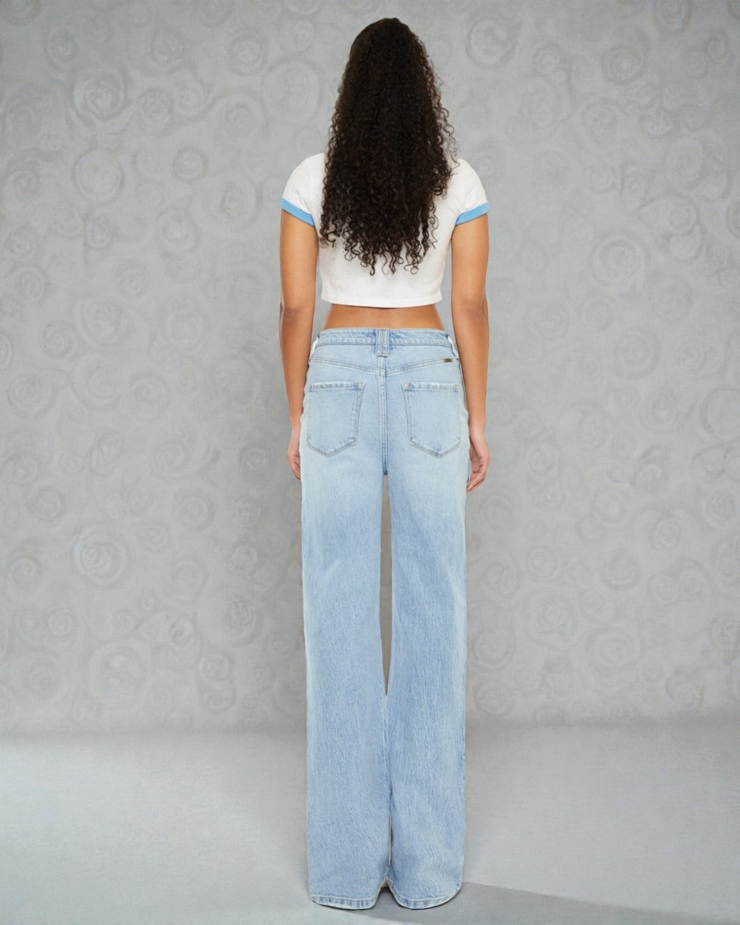 Person wearing a white crop top and light blue jeans against a gray textured wall.