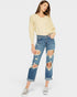 Woman wearing a light yellow sweater and distressed blue jeans on a white background
