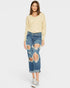 Woman wearing a light yellow sweater and distressed blue jeans on a white background