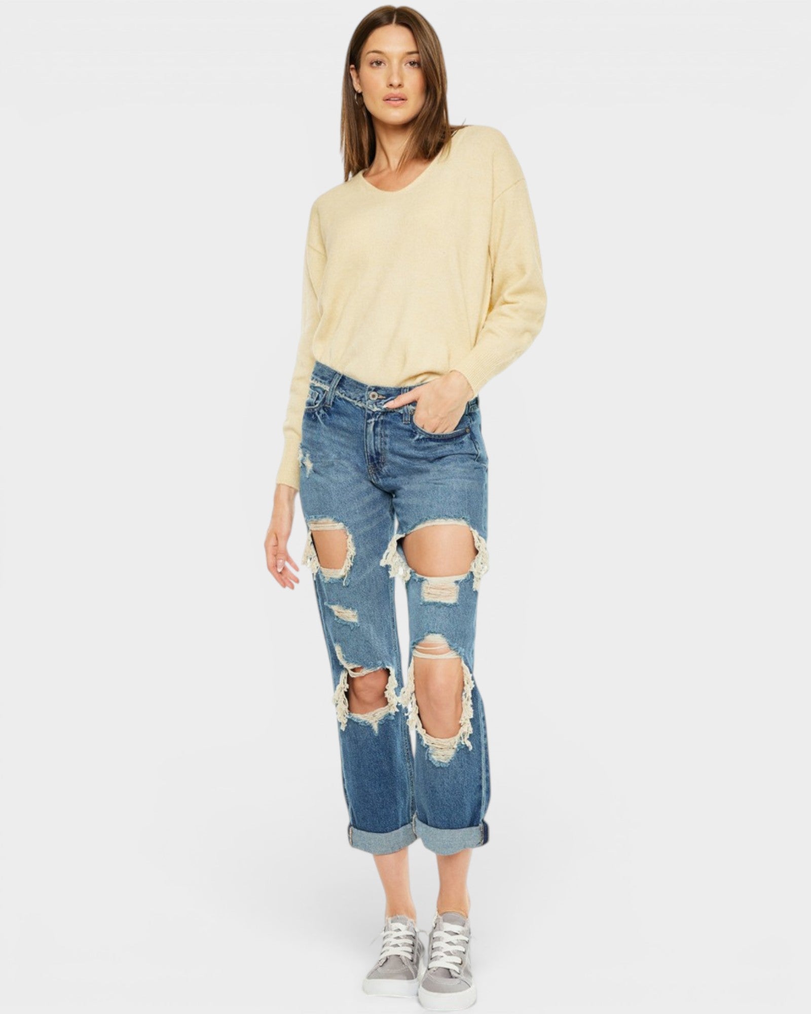 Woman wearing a light yellow sweater and distressed blue jeans on a white background