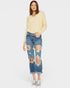 Woman wearing a light yellow sweater and distressed blue jeans on a white background