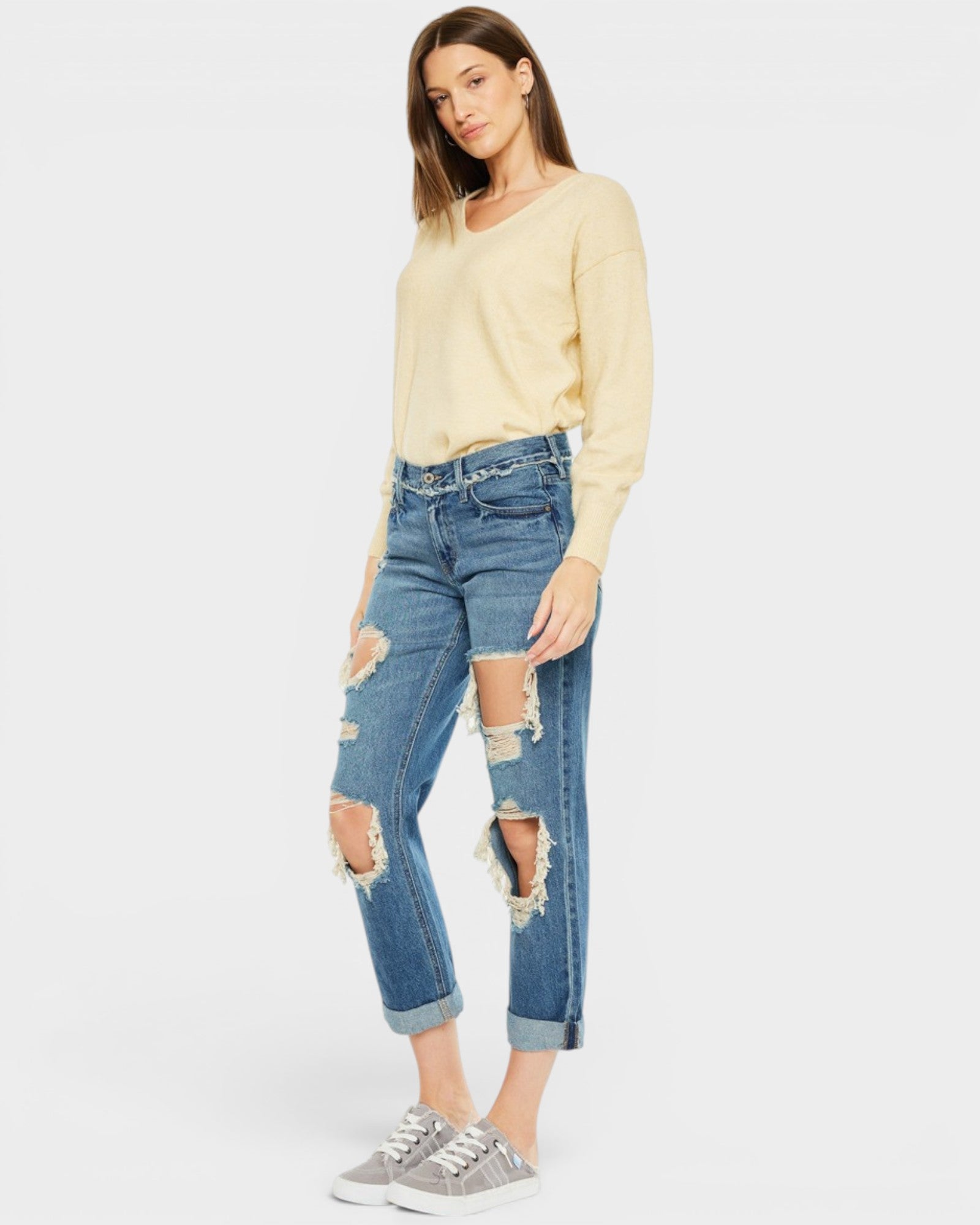 Woman wearing a yellow sweater and distressed blue jeans on a white background