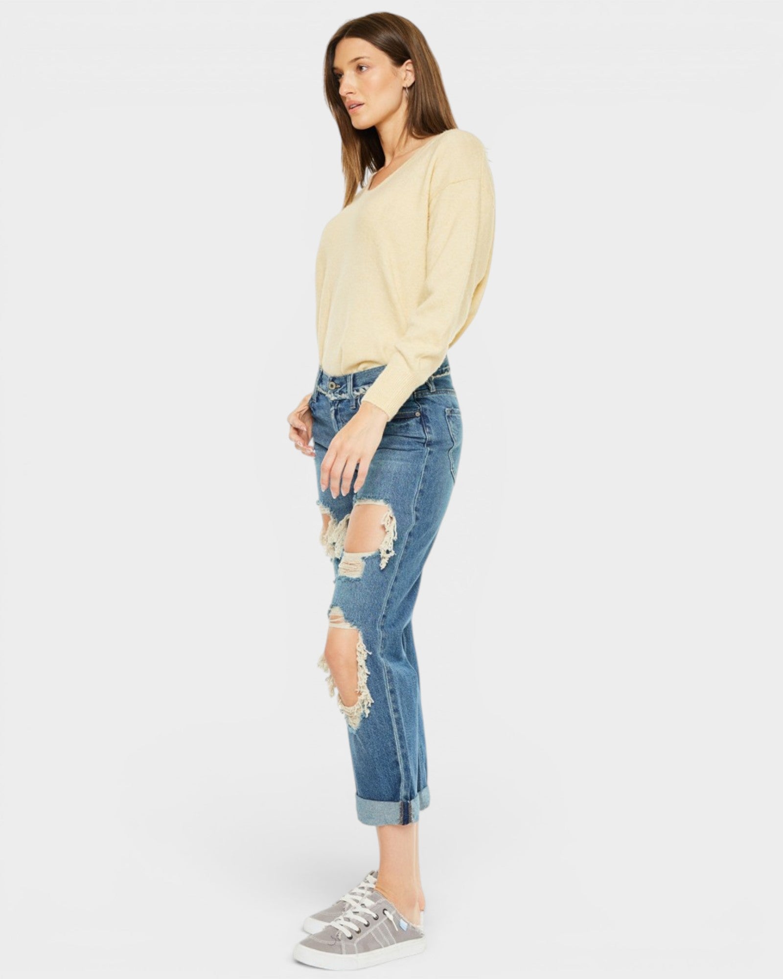 Woman wearing a light yellow sweater and distressed blue jeans on a white background
