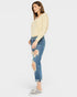 Woman wearing a light yellow sweater and distressed blue jeans on a white background