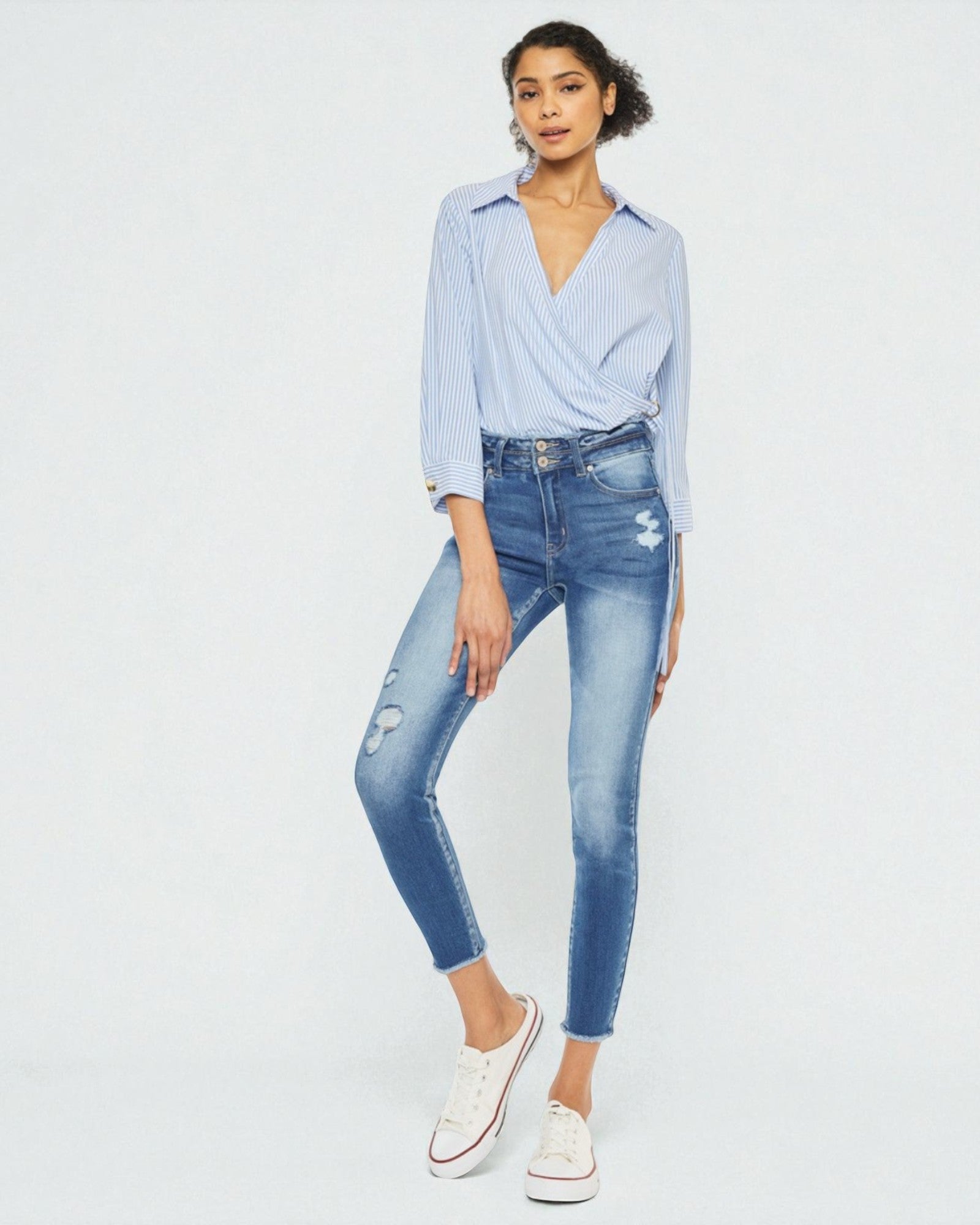 Woman wearing a light blue shirt and ripped jeans on a white background
