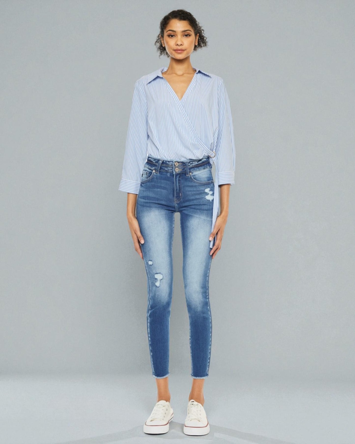 Woman wearing a light blue striped shirt and distressed jeans on a gray background