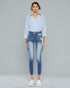 Woman wearing a light blue striped shirt and distressed jeans on a gray background