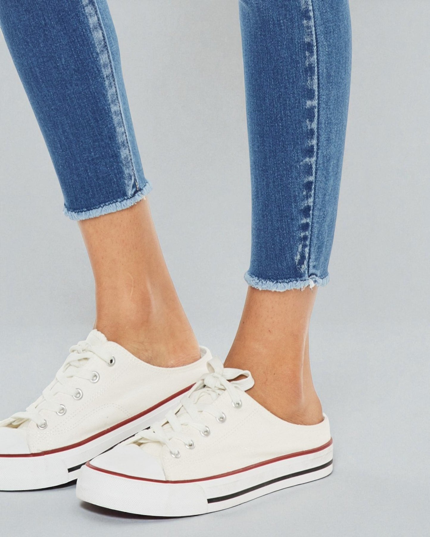 White sneakers with red accents worn with blue jeans on a gray background