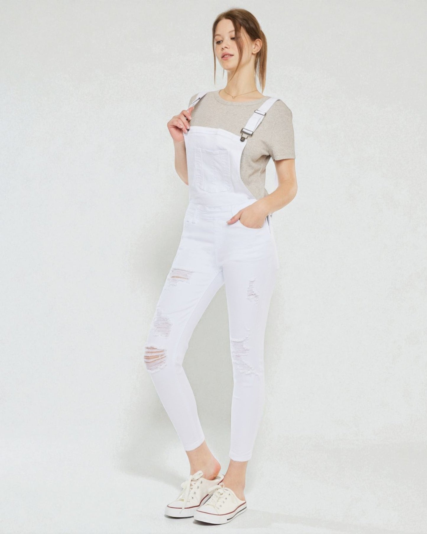 Person wearing a gray t-shirt and white ripped overalls on a plain background