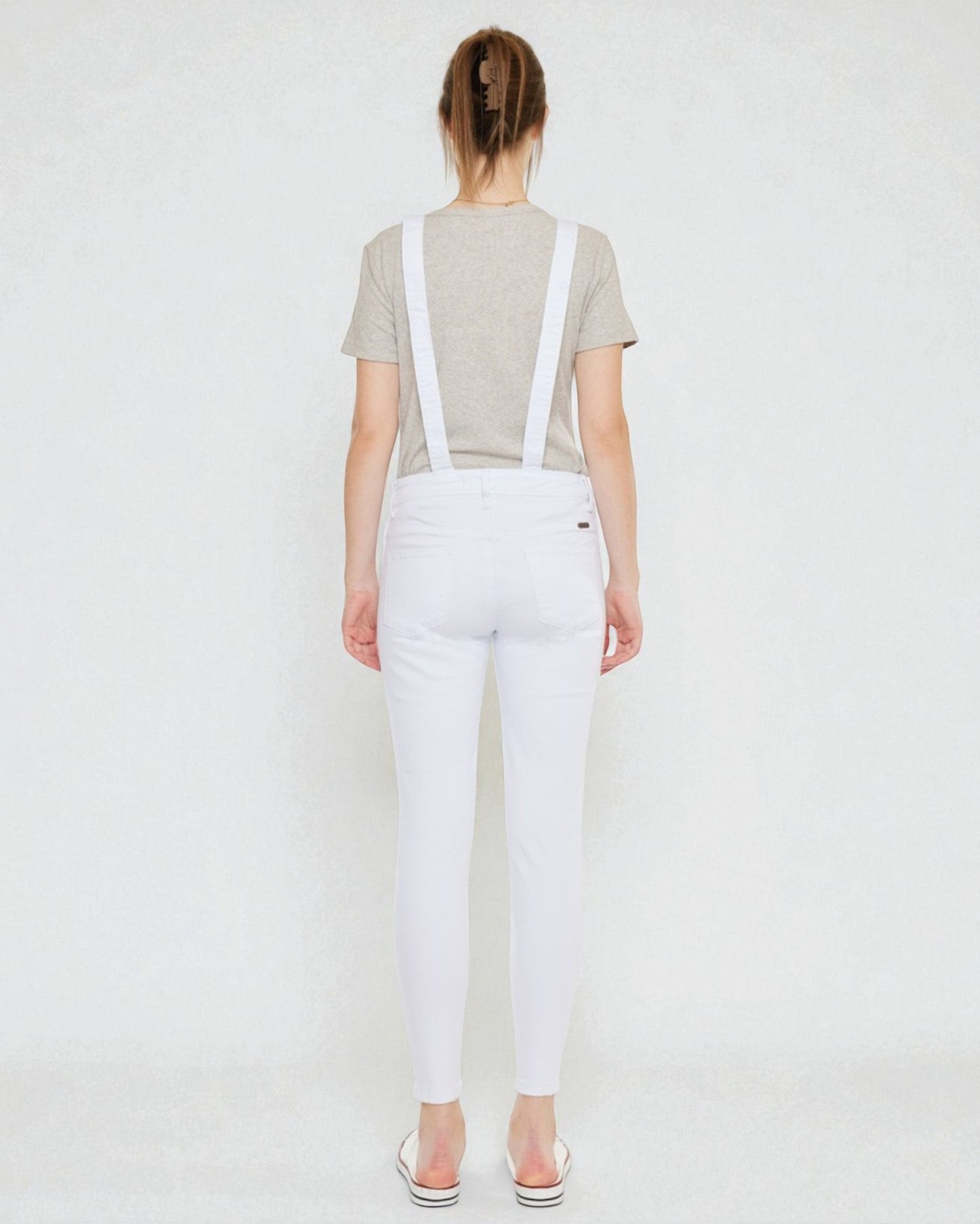 Person wearing white overalls with suspenders on a plain background