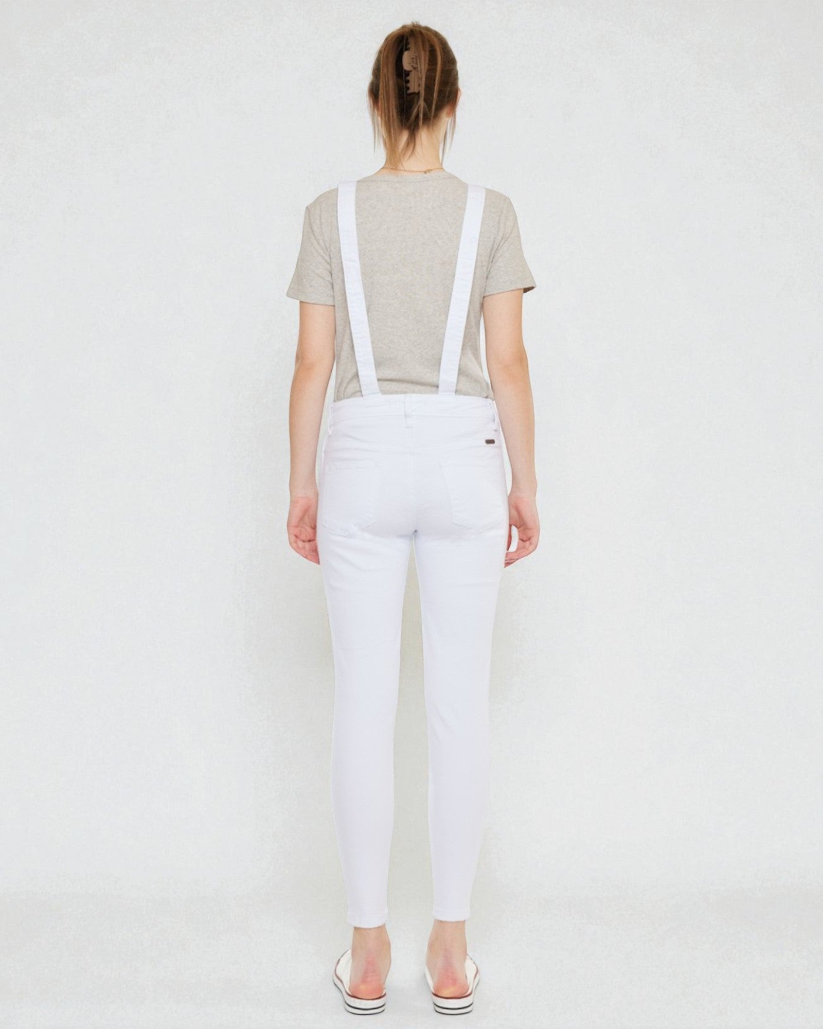 Person wearing white overalls with suspenders on a plain background