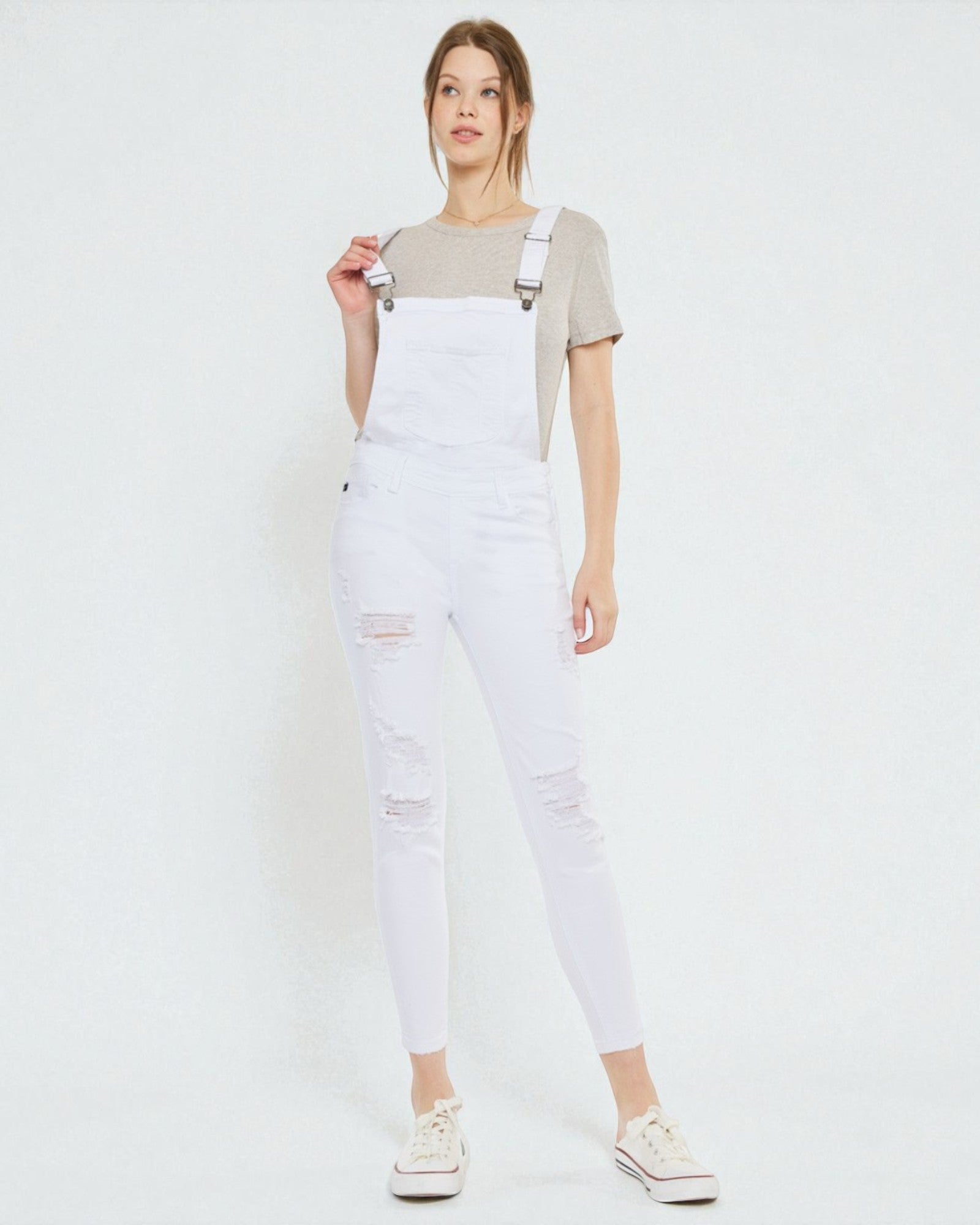 Person wearing white denim overalls on a plain background
