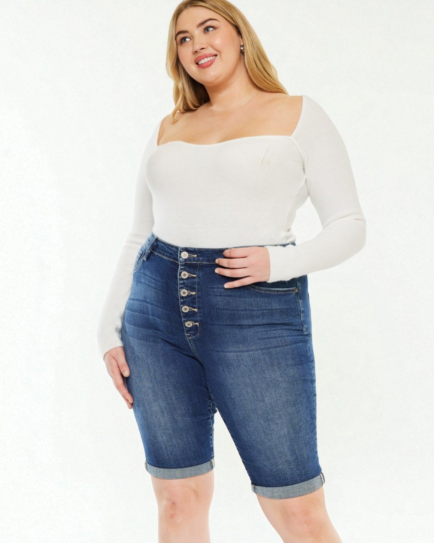 Woman wearing a white long-sleeve top and blue denim shorts on a white background