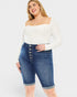 Woman wearing a white long-sleeve top and blue denim shorts on a white background