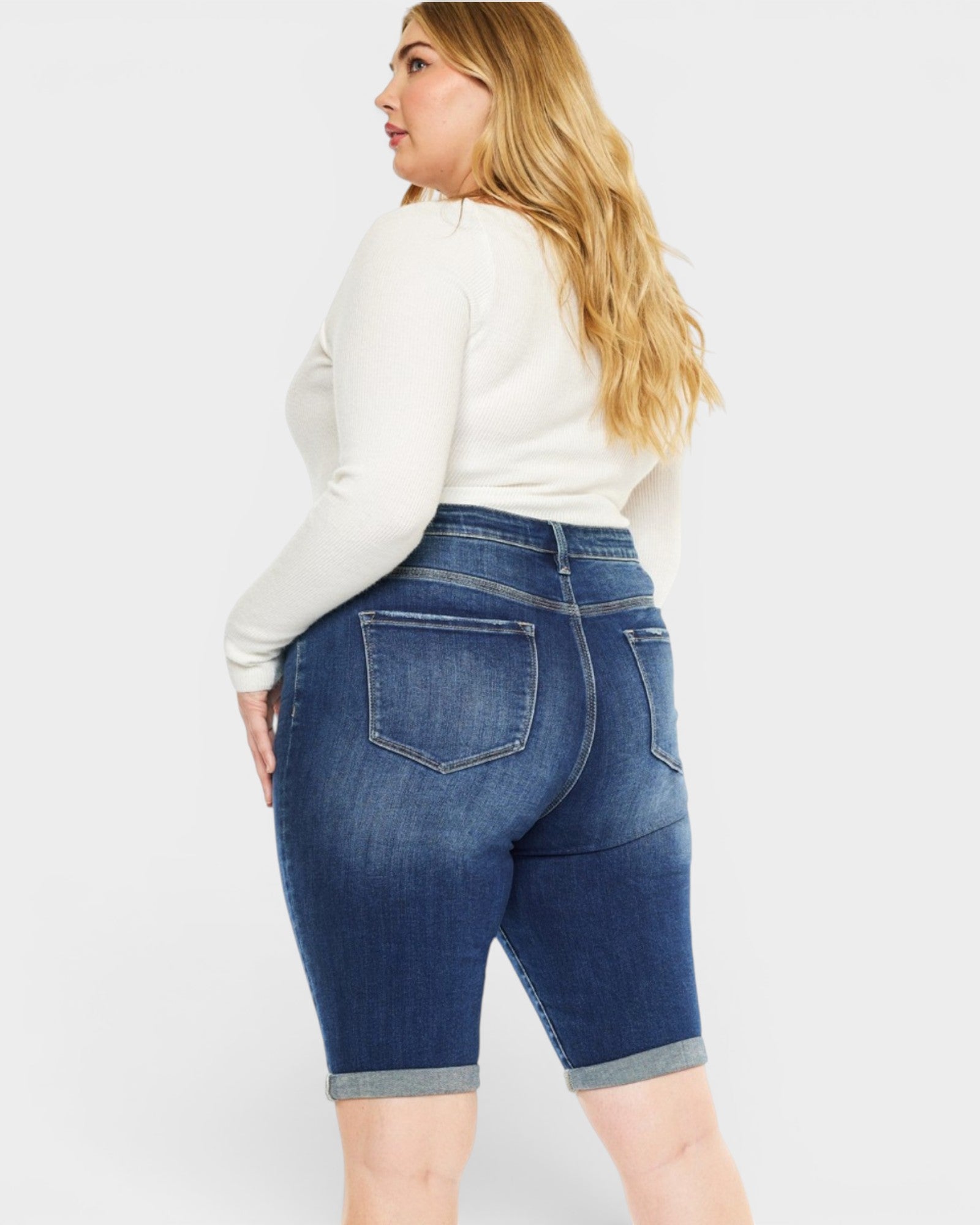 Woman wearing blue denim shorts and a white long-sleeve shirt on a white background