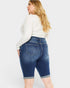 Woman wearing blue denim shorts and a white long-sleeve shirt on a white background