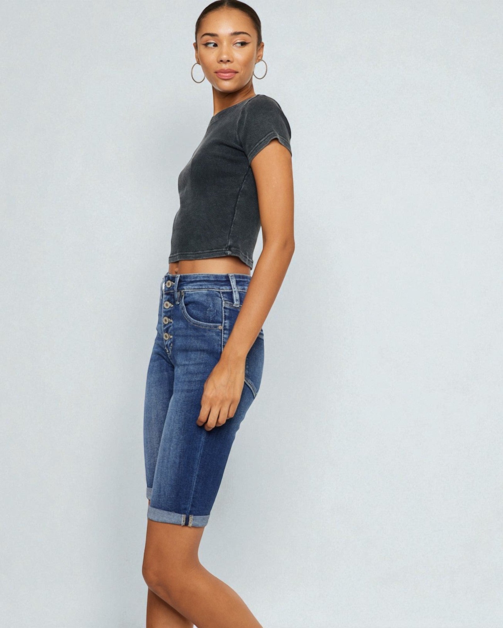 Woman wearing a dark gray crop top and blue denim shorts on a light gray background