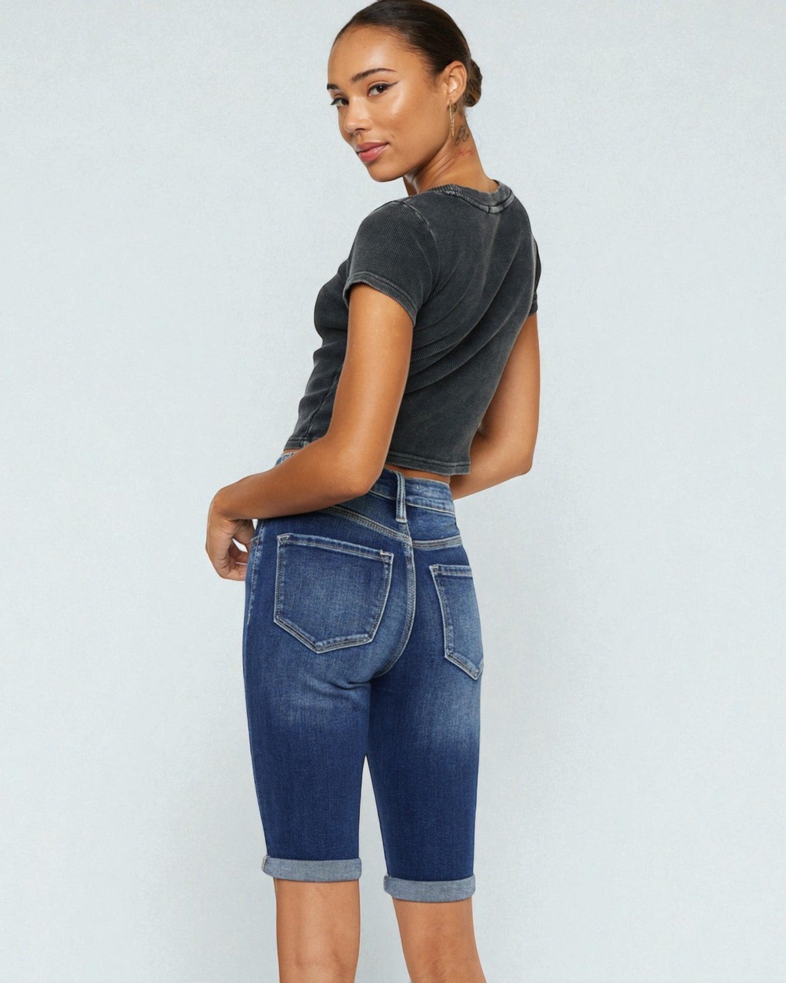 Woman wearing a dark gray t-shirt and blue denim shorts on a light gray background