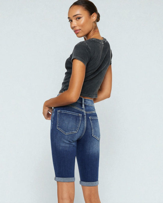 Woman wearing a dark gray t-shirt and blue denim shorts on a light gray background